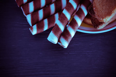 Striped chocolate wafer rolls on plate on black wooden background. Toned.