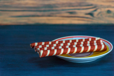 Striped wafer rolls on a plate on a wooden backgroundの写真素材