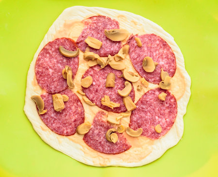 Pizza with salami and mushrooms on a green background, top viewの写真素材