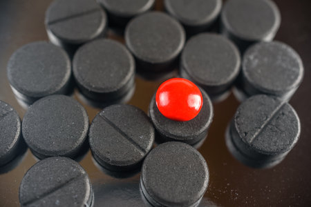 Close up of red pill on pile of black pills on black backgroundの写真素材