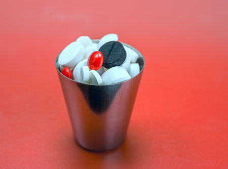 Pills in a silver cup on a red background. Close-up.の写真素材
