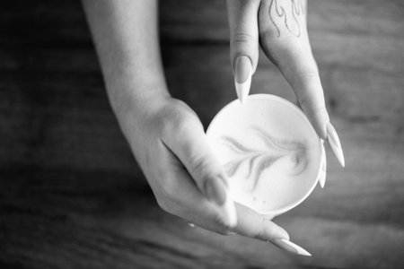 Hands holding a white cup of latte art with intricate designs, showing creamy texture and warm colors, creating a cozy coffee experience with artistic flairの写真素材