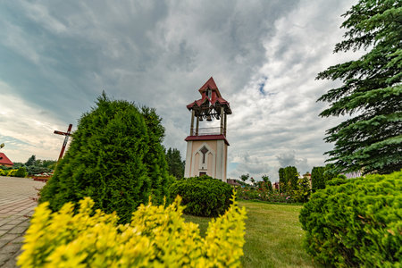 Beautiful modern church with a unique architectural design, featuring a prominent steeple, surrounded by vibrant flowers and lush greenery, under a dramatic cloudy skyの写真素材