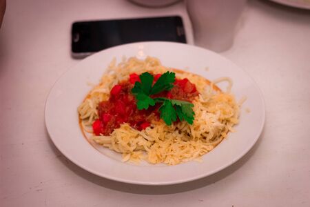plate with italian spaghetti, sauce and basil on white table