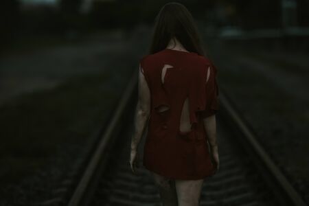 girl in torn red clothes on the railroad dirt on the body dark tones violence themeの写真素材