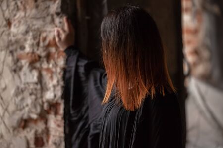 red-haired girl in a black dress by the window of a ruined building with red brick wallsの写真素材