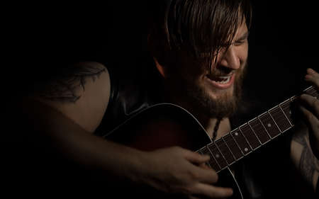 Brutal bearded man with a cigarette in a recording Studio with guitar on the black background local...