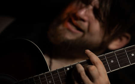 Brutal bearded man with a cigarette in a recording Studio with guitar on the black background local lightの写真素材