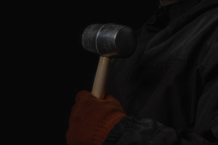 The hand holds a rubber mallet with a wooden handle lose up Isolated on a black backgroundの写真素材