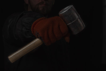 The hand holds a rubber mallet with a wooden handle lose up Isolated on a black backgroundの写真素材