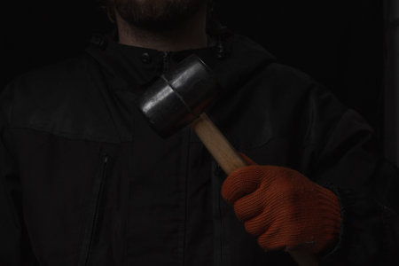 The hand holds a rubber mallet with a wooden handle lose up Isolated on a black backgroundの写真素材