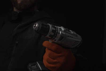 Hand holds cordless electric screwdriver with bit for screws and drilling isolated on black...