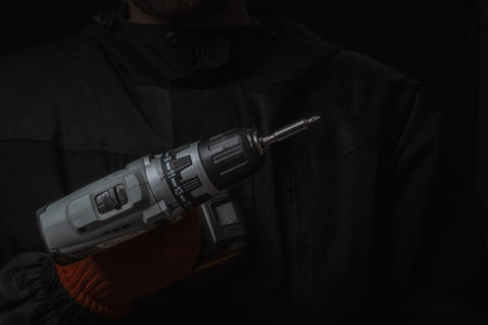 Hand holds cordless electric screwdriver with bit for screws and drilling isolated on black...