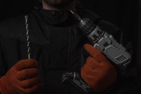 Hand holds cordless electric screwdriver with bit for screws and drilling isolated on black backgroundの写真素材