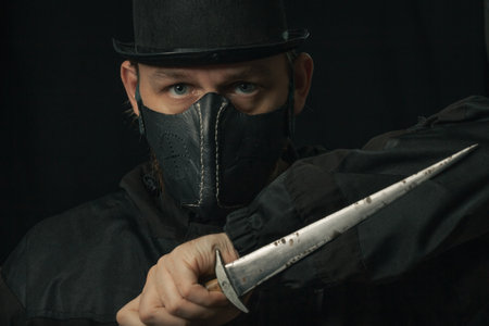 Scary man with knife or dagger creepy mask and hat in the darkの写真素材