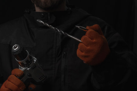 Hand holds cordless electric screwdriver with bit for screws and drilling isolated on black...