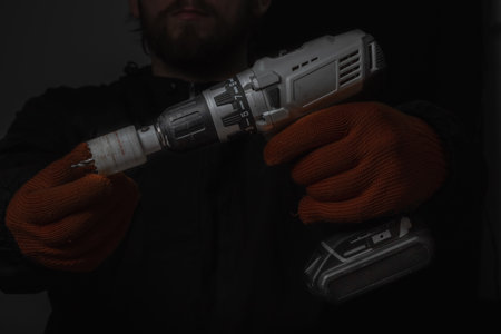 Hand holds cordless electric screwdriver with bit for screws and drilling isolated on black backgroundの写真素材