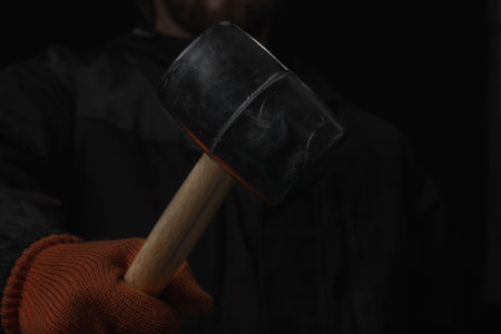 The hand holds a rubber mallet with a wooden handle lose up Isolated on a black background
