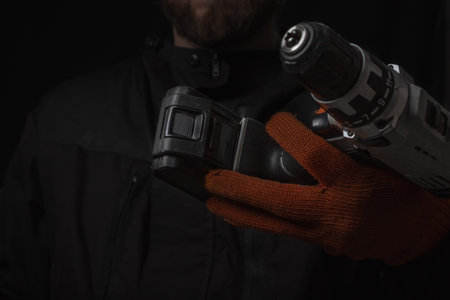 Hand holds cordless electric screwdriver with bit for screws and drilling isolated on black backgroundの写真素材