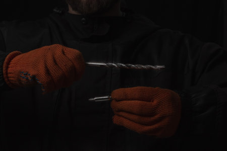 Hand holds cordless electric screwdriver with bit for screws and drilling isolated on black backgroundの写真素材