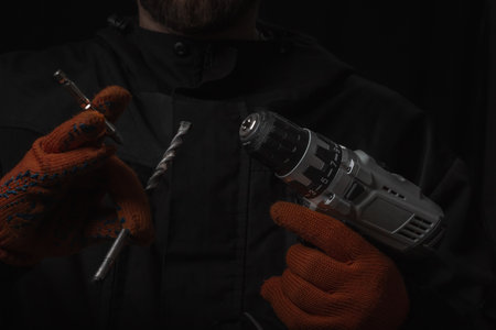 Hand holds cordless electric screwdriver with bit for screws and drilling isolated on black...