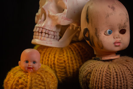 Yellow-orange pumpkins with broken cracked doll head candles and skulls on a black background the concept of Halloween and the autumn harvest of pumpkin close-up copyspace from aboveの写真素材