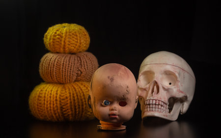 Yellow-orange pumpkins with broken cracked doll head candles and skulls on a black background the...