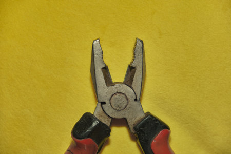 Pliers Open metal nippers with a red handle isolated on yellow background