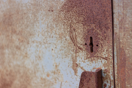 a keyhole on an old rusty safe standing on the street near a white brick wall on the asphalt next to...