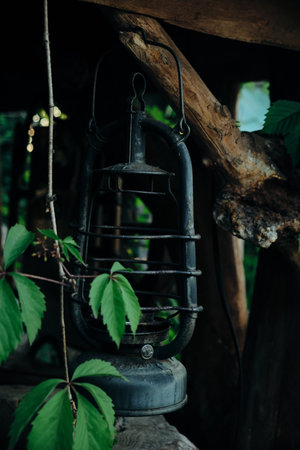 An old kerosene lamp hanging from a wooden beam or window on a rusty vintage hookの写真素材