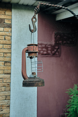 An old kerosene lamp hanging from a wooden beam or window on a rusty vintage hookの写真素材