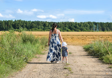 A young mother and her daughter walk along a country road to a wheat field in the summerの写真素材