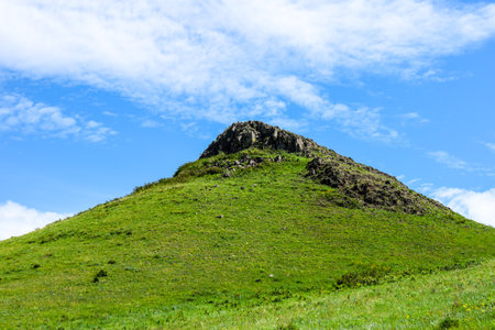 Mountain landscape with green grass, blue sky and white clouds. Paleovolcano surroundings,...
