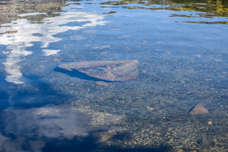 blue water surface with reflection of clouds and rocks in the water. Ergaki Nature Park, Krasnoyarsk...