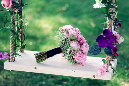 Wedding bouquet of peonies lying on a swing decorated with fresh flowersの写真素材
