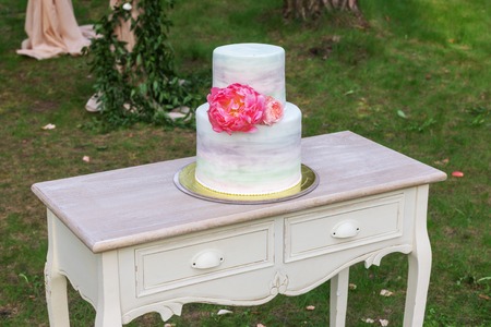 Vintage wooden table with the wedding cake standing on a green lawn. Cake decorated with fresh peoniesの写真素材