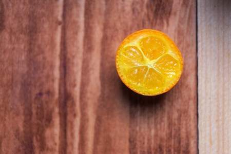 Macro image background of a slice kumquat. One piece lies on a wooden table.