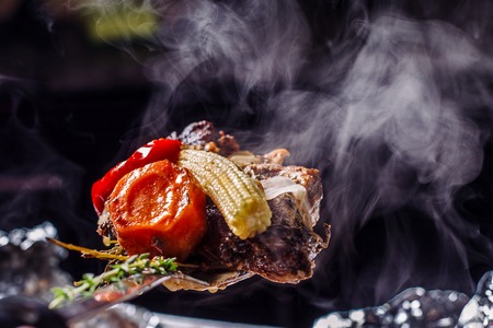 Hot meat on a spoon, with corn cob, carrot and pepper. Steam on a black background.の写真素材