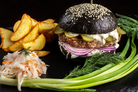 Black hamburger with onions and cucumbers on stone table with black background.の写真素材