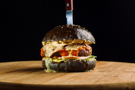 Close-up of delicious fresh home made beef burger with lettuce, cheese, onion and tomato. Hangs a corner of cheese. Black bun.の写真素材