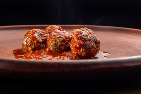 Meatballs with glaze lie on a clay plate on black background.の写真素材