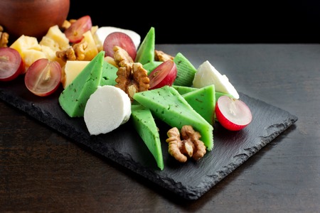 Cheese plate on black shale. Pieces of fruit.の写真素材