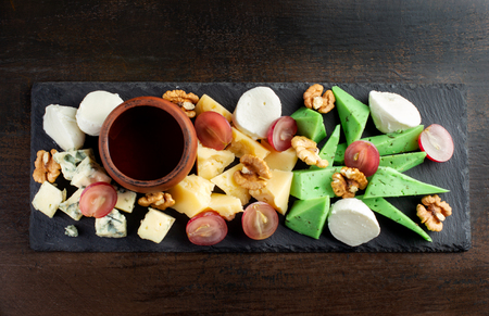 Cheese plate on black shale. Pieces of fruit.の写真素材