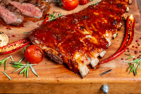 Ribs on the board. Close-up, beautiful pepper and rosemary are nearby.の写真素材
