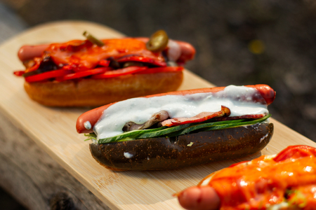 Black hotdog with salad, bacon, sour cream sauce, on wooden board.の写真素材
