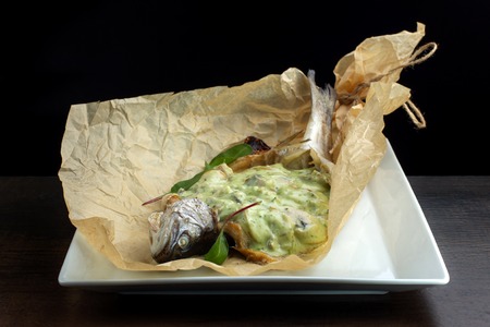 Stuffed fish wrapped in kraft paper. On white plate.の写真素材