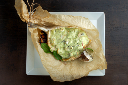 Stuffed fish wrapped in kraft paper. On white plate.の写真素材