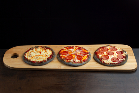 Creative pizza on black dough, three pieces on the board.の写真素材