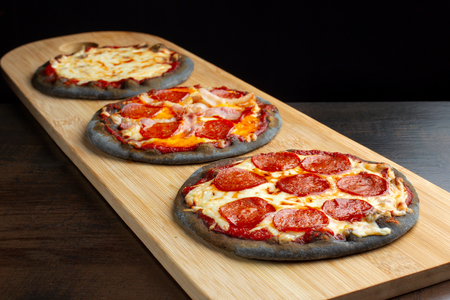 Creative pizza on black dough, three pieces on the board.の写真素材