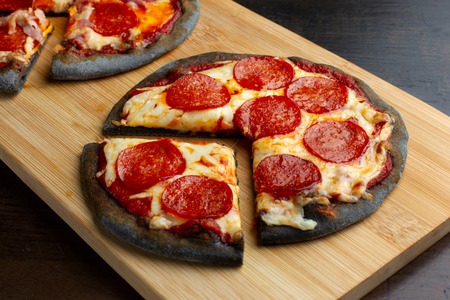 Creative pizza on black dough, three pieces on the board.の写真素材